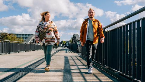Zwei junge Erwachsene laufen bei Sonnenschein über den Fußweg am RS1, beide lächeln motiviert.