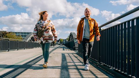 Zwei junge Erwachsene laufen bei Sonnenschein über den Fußweg am RS1, beide lächeln motiviert.