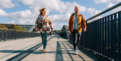 Zwei junge Erwachsene laufen bei Sonnenschein über den Fußweg am RS1, beide lächeln motiviert.