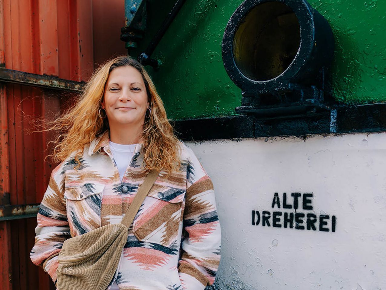 Frau lehnt sich an einen bunten Zug, auf dem „Alte Dreherei” steht, und lächelt fröhlich in die Kamera.