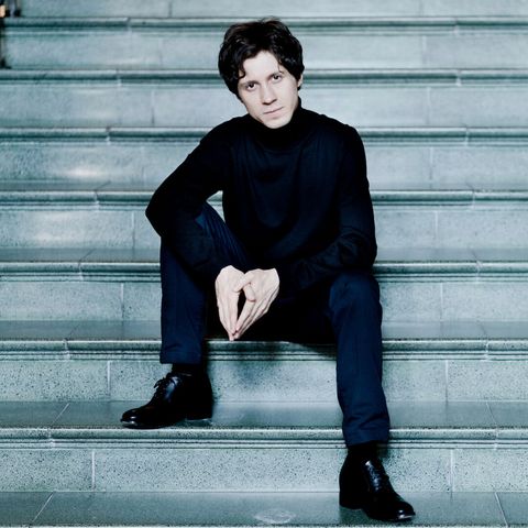 Pianist Rafał Blechacz sitzt in schwarzer Kleidung auf einer Stein-Treppe.