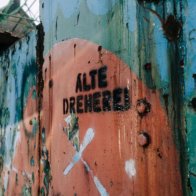 Schwarzes Graffiti mit der Aufschrift „Alte Dreherei” an einer Stahl-Fassade