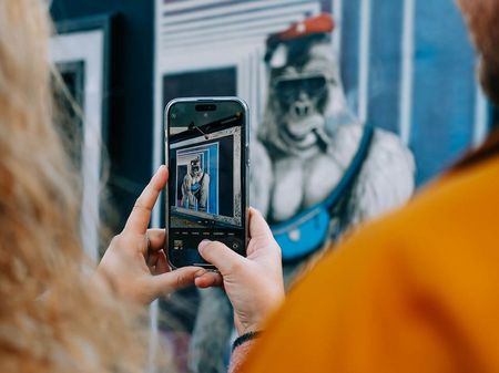 Zwei Erwachsene fotografieren mit dem Smartphone ein Kunstwerk an einer Hauswand.