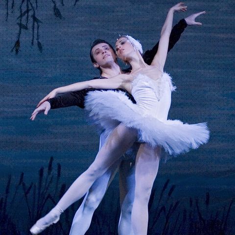 Zwei Ballett-Tänzer tanzen Schwanensee auf einer blau beleuchteten Bühne.