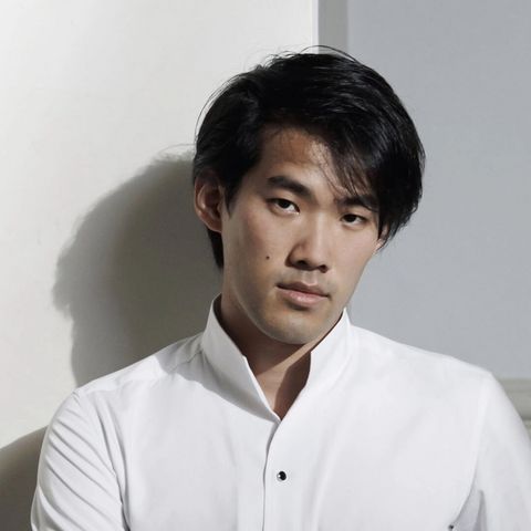 Porträt von Bruce Liu in einem weißen Hemd vor einer hellen Wand.