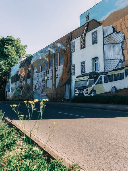 Blick über eine breite Straße auf eine Hauswand, die mit bunter Street Art bemalt ist.