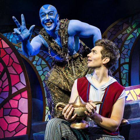 Dschinni, der blaue Geist aus der Wunderlampe, hebt fröhlich und voller Energie drei Finger in die Luft. Aladin hält die Wunderlampe und blickt fasziniert auf die drei Finger.