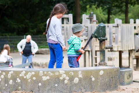 Kinder an der Wasserpumpe im Sommer auf dem Matschspielplatz im Darlington Park in Mülheim an der Ruhr 