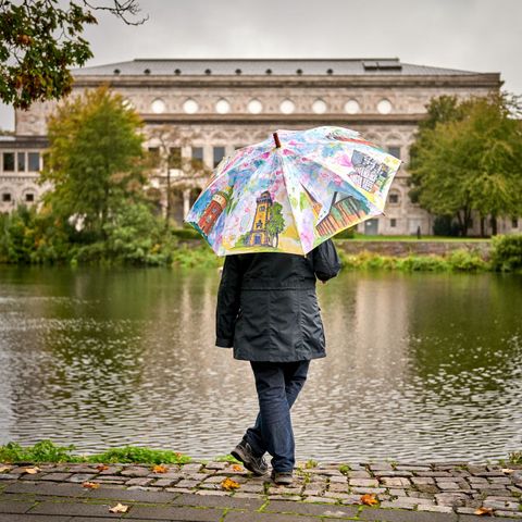 Frau mit Mülheim-Regenschirm im Herbst an der Ruhr mit Blick auf die Stadthalle Mülheim