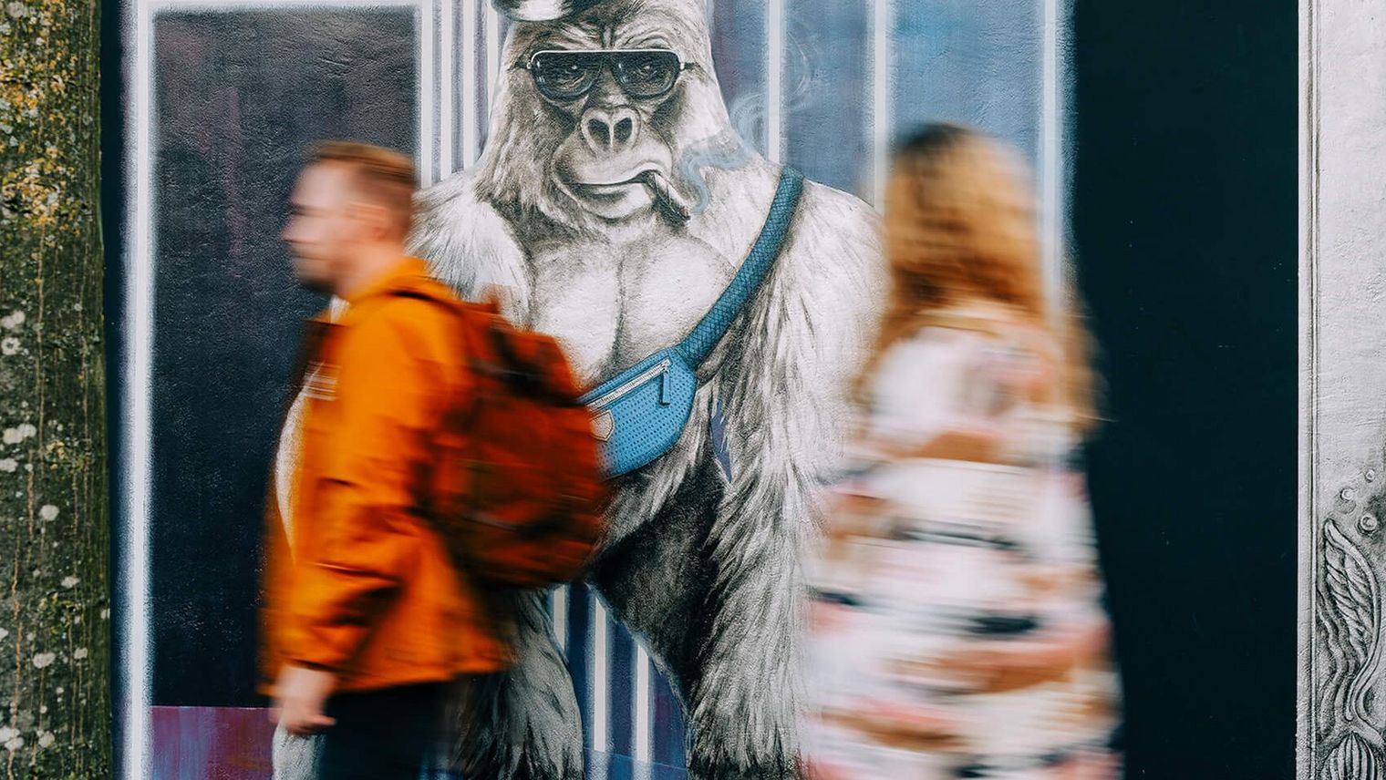 Zwei junge Erwachsene laufen an einer Hauswand mit einem gemalten Gorilla vorbei. Die Frau blickt zum Kunstwerk. 